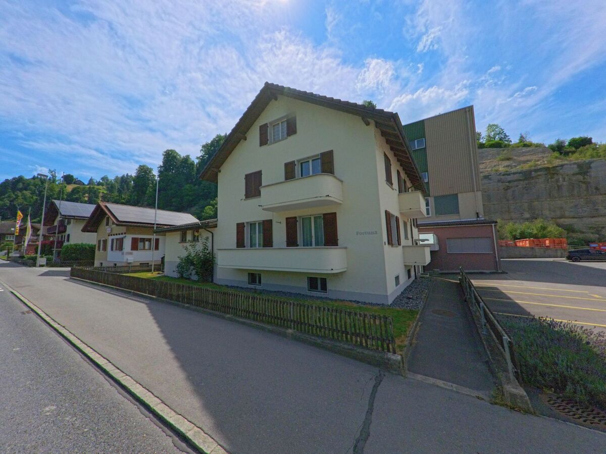 In Wolhusen (6110, Kanton Luzern) reihen sich Ein- und Mehrfamilienhäuser entlang einer ruhigen Strasse am Fuss einer bewaldeten Felswand.