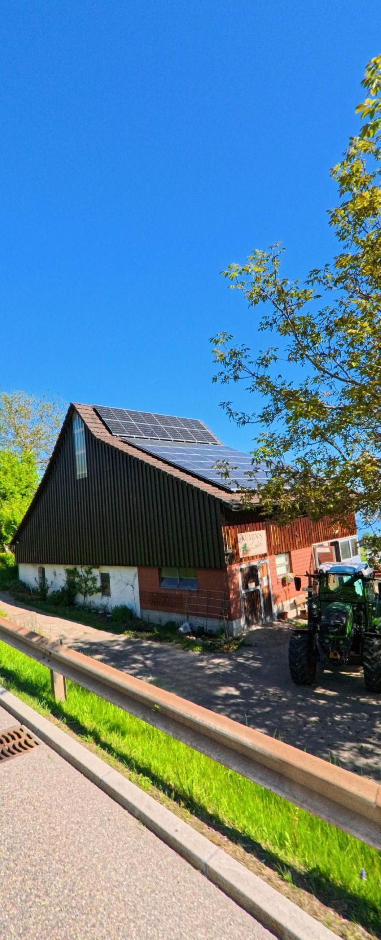 Ein landwirtschaftliches Gebaeude mit Photovoltaikanlage auf dem Dach steht in Wollerau (8832, Kanton Schwyz) neben einer Strasse, waehrend ein Traktor im Vordergrund parkt.