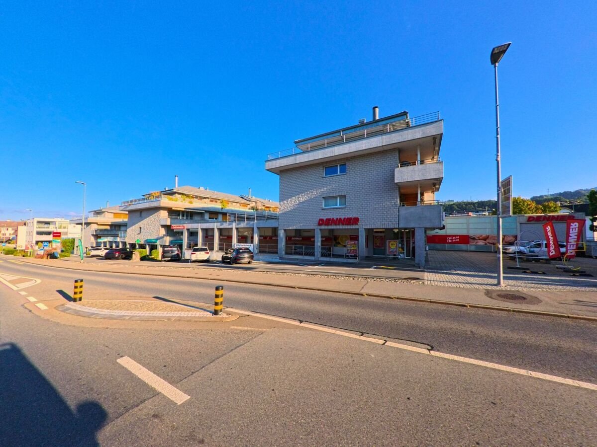 Entlang der Hauptstrasse in Wollerau (8832, Kanton Schwyz) stehen moderne Gewerbe- und Wohngebaeude, deren Fassaden von breiten Balkonen und grossen Fensterfronten gepraegt sind.