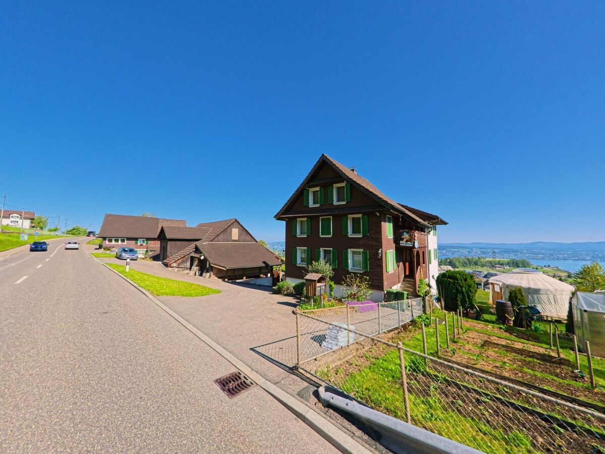 Oberhalb des Sees liegt in Wollerau (8832, Kanton Schwyz) ein traditionelles Wohnhaus mit gruener Umgebung direkt an einer leicht ansteigenden Strasse.