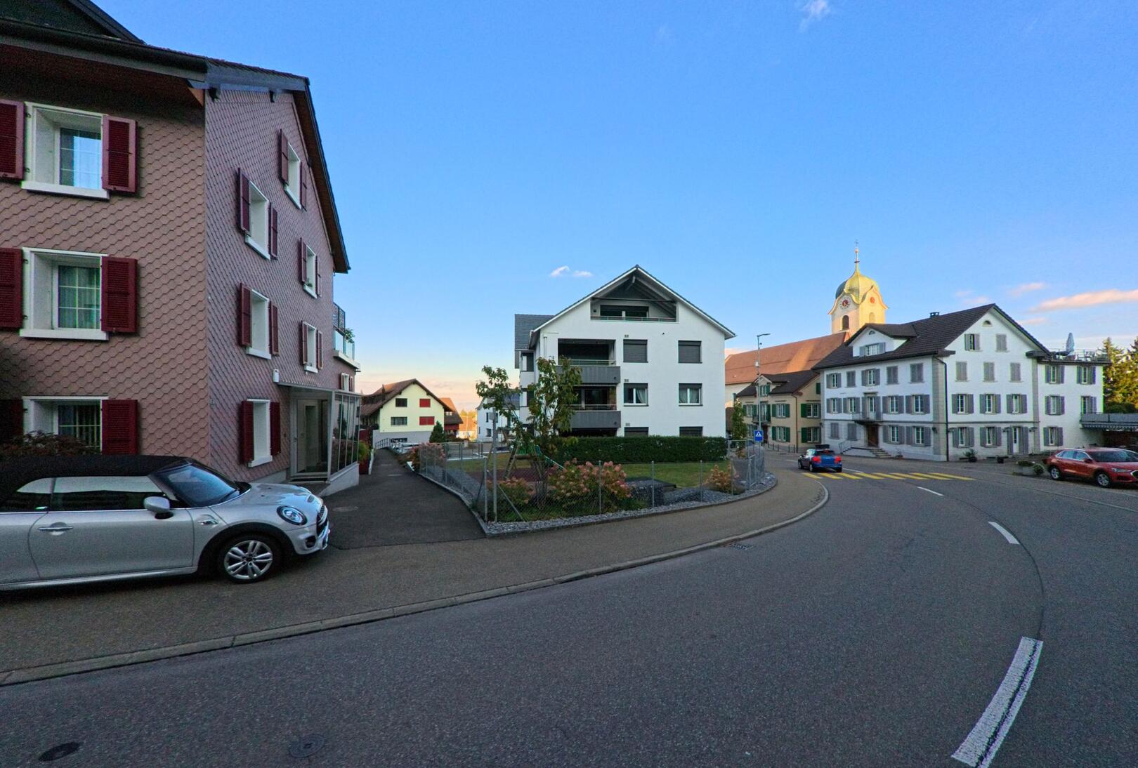 In einer ruhigen Strassenszene in Wollerau (8832, Kanton Schwyz) saeumen Wohnhaeuser mit unterschiedlichen Fassaden die leicht geschwungene Fahrbahn.