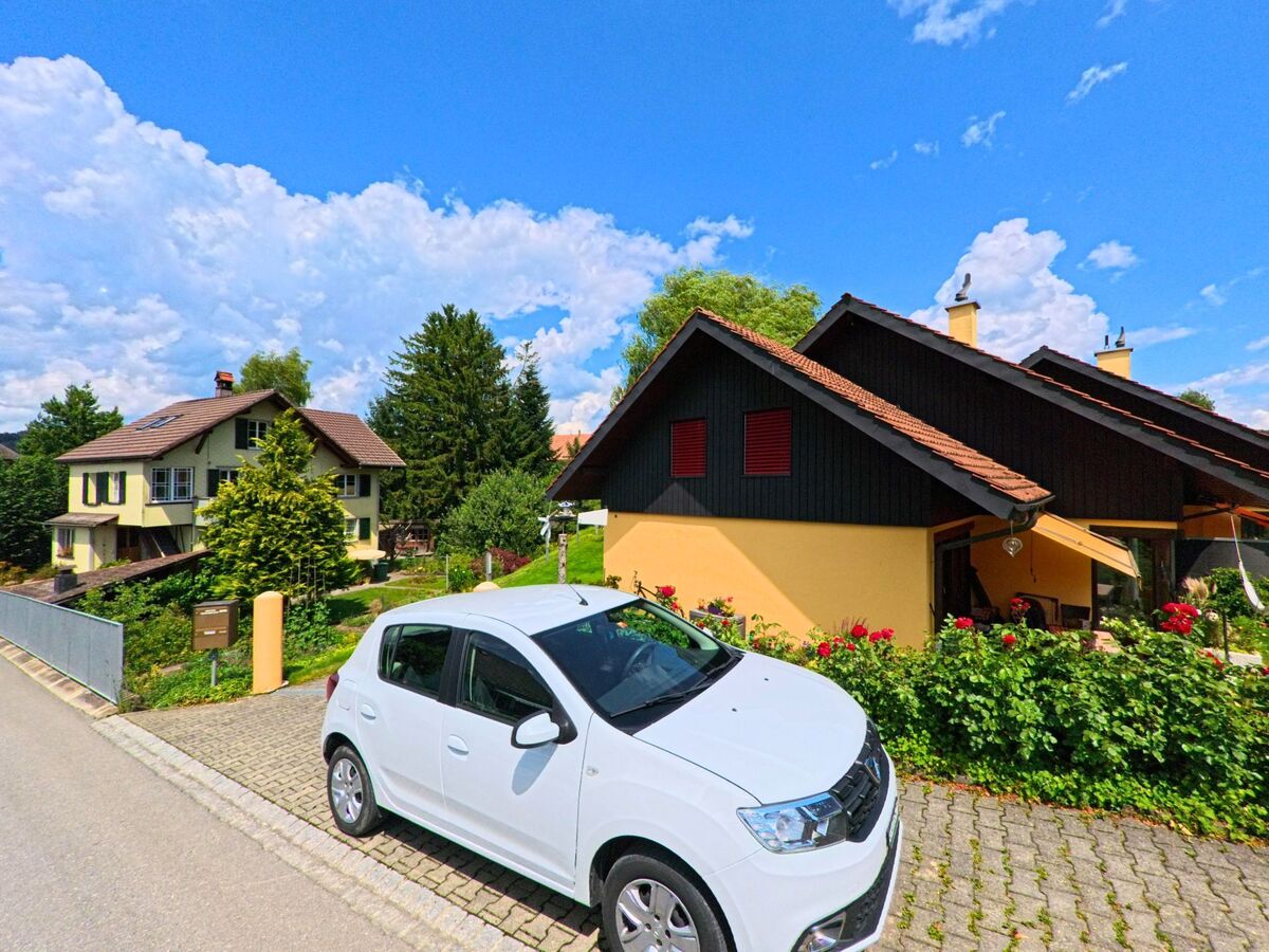 In einem Wohngebiet von Worb (3076, Kanton Bern) reihen sich gepflegte Einfamilienhäuser mit blühenden Vorgärten und einem geparkten weissen Auto an der Strasse.