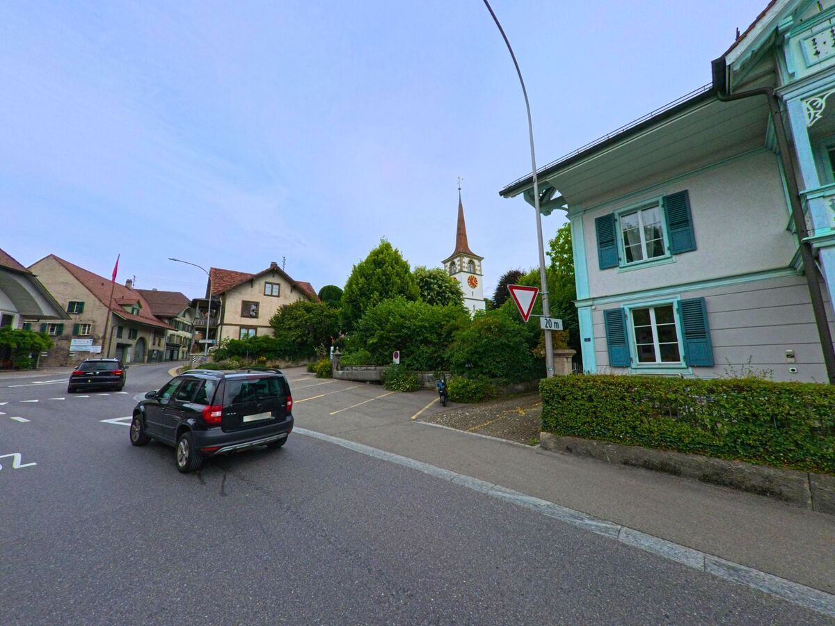 Im historischen Zentrum von Worb (3076, Kanton Bern) ragt der markante Kirchturm über die Dächer traditioneller Wohnhäuser an einer belebten Strassenecke empor.