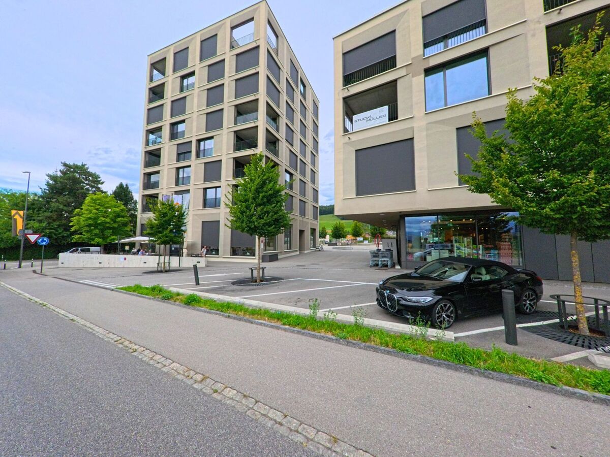 Zwei moderne Wohn- und Geschäftsbauten in Worb (3076, Kanton Bern) stehen sich gegenüber, dazwischen ein Parkplatz und ein Supermarkt im Erdgeschoss.