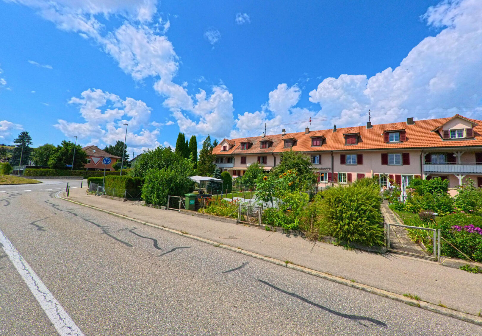 Entlang einer ruhigen Wohnstrasse in Worb (3076, Kanton Bern) stehen gepflegte Reihenhäuser mit liebevoll angelegten Vorgärten und leuchtenden Sonnenblumen.