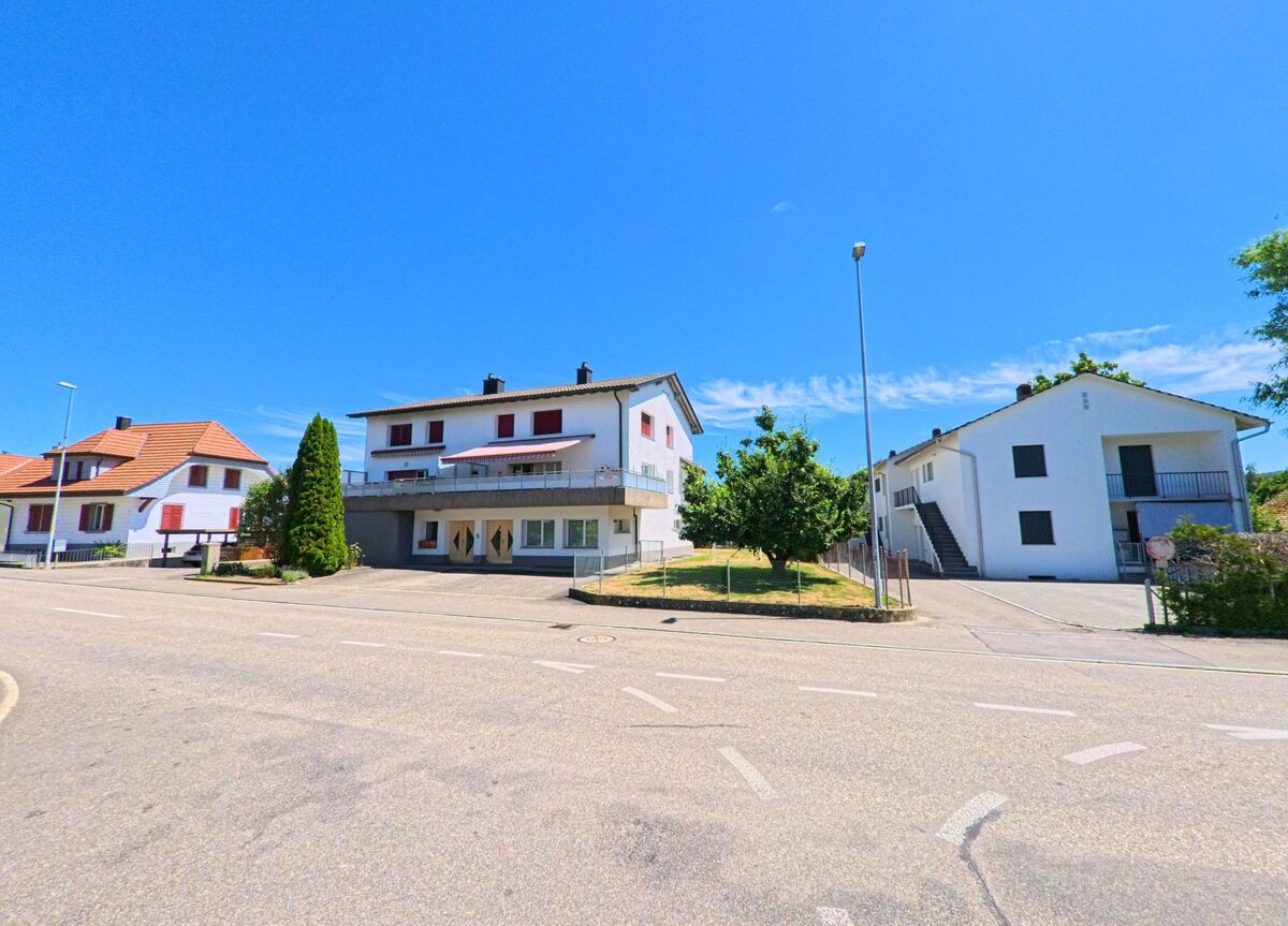In Wynau (4923, Kanton Bern) stehen mehrere Wohnhaeuser mit Balkonen und farblich abgestimmten Fensterlaeden entlang einer verkehrsberuhigten Strasse.