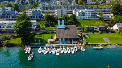 In Horgen (8810, Kanton Zürich) liegt der Yacht Club direkt am Ufer, wo mehrere Segelboote vor einem modernen Gebäude vertäut sind und eine grüne Wiese das Gelände schmückt.