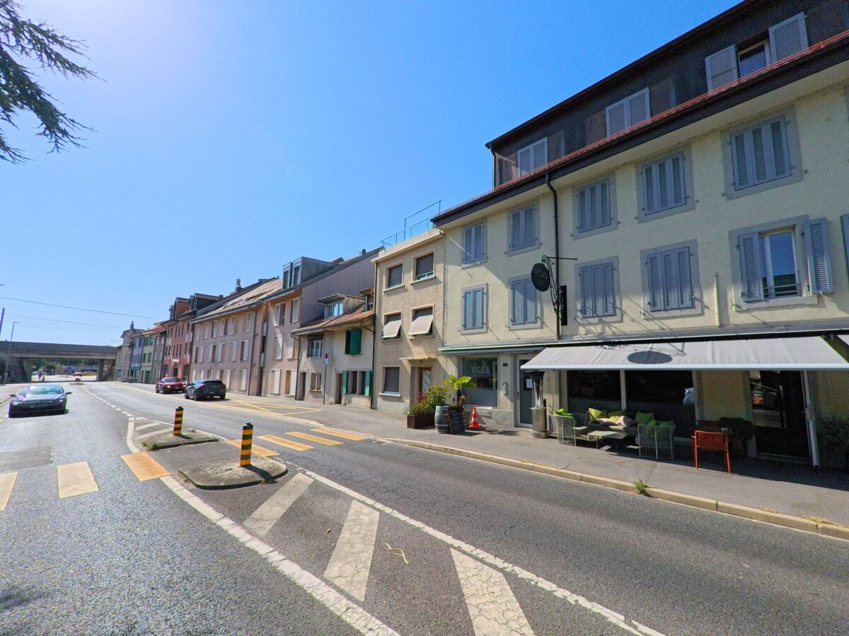 In Yverdon-les-Bains (1400, Kanton Waadt) reihen sich mehrstöckige Wohnhaeuser mit Laeden und einem Restaurant entlang einer breiten Strasse.