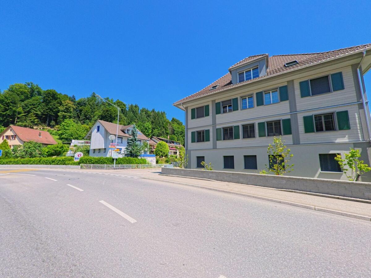  Im Zentrum von Zell (6144, Kanton Luzern) stehen moderne und traditionelle Wohnhäuser direkt an einer leicht gebogenen Strasse mit angrenzendem Wald.