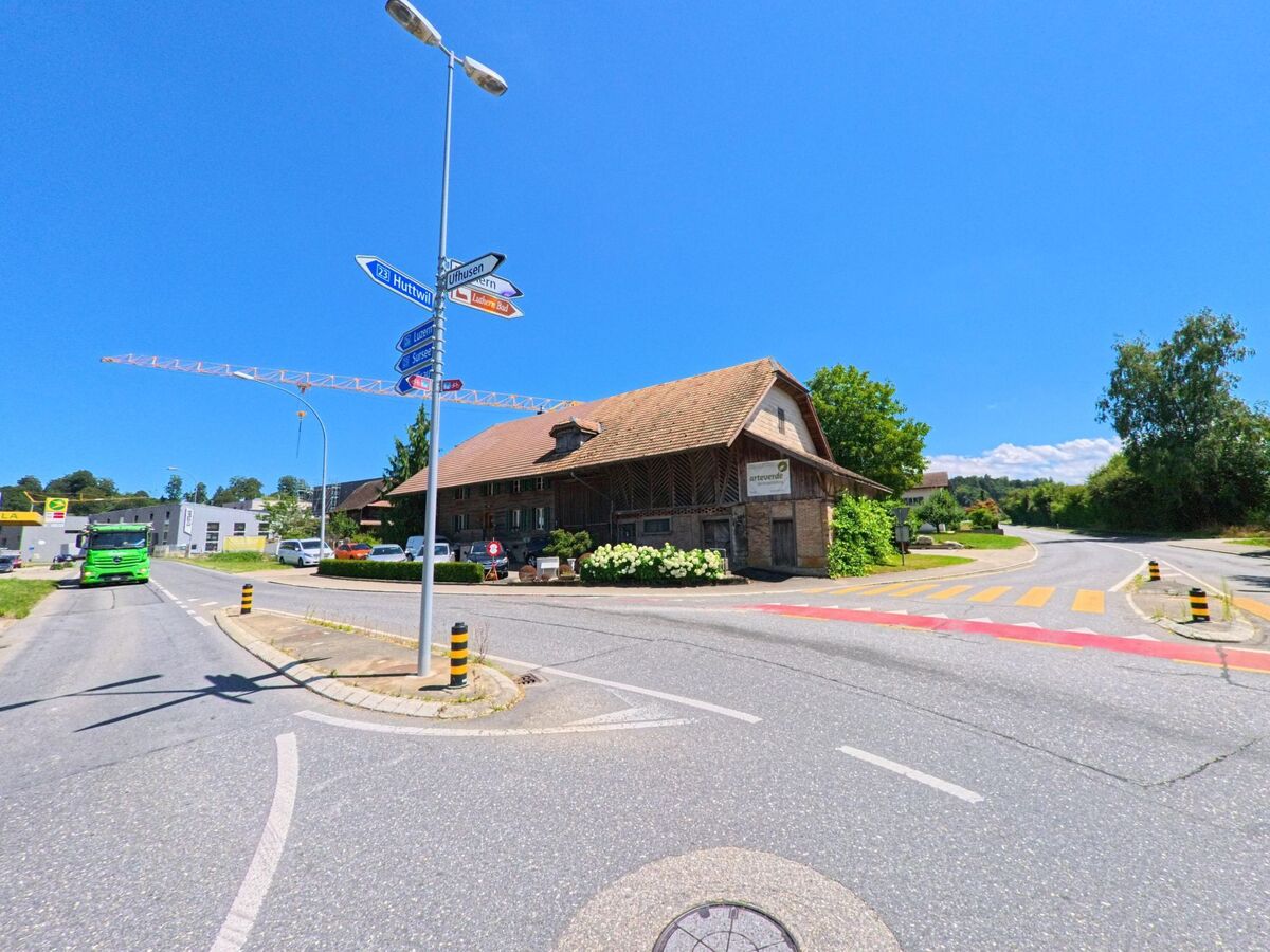 In Zell (6152, Kanton Luzern) trifft eine Strassenkreuzung mit mehreren Wegweisern auf ein traditionelles Bauernhaus mit Schindelfassade.
