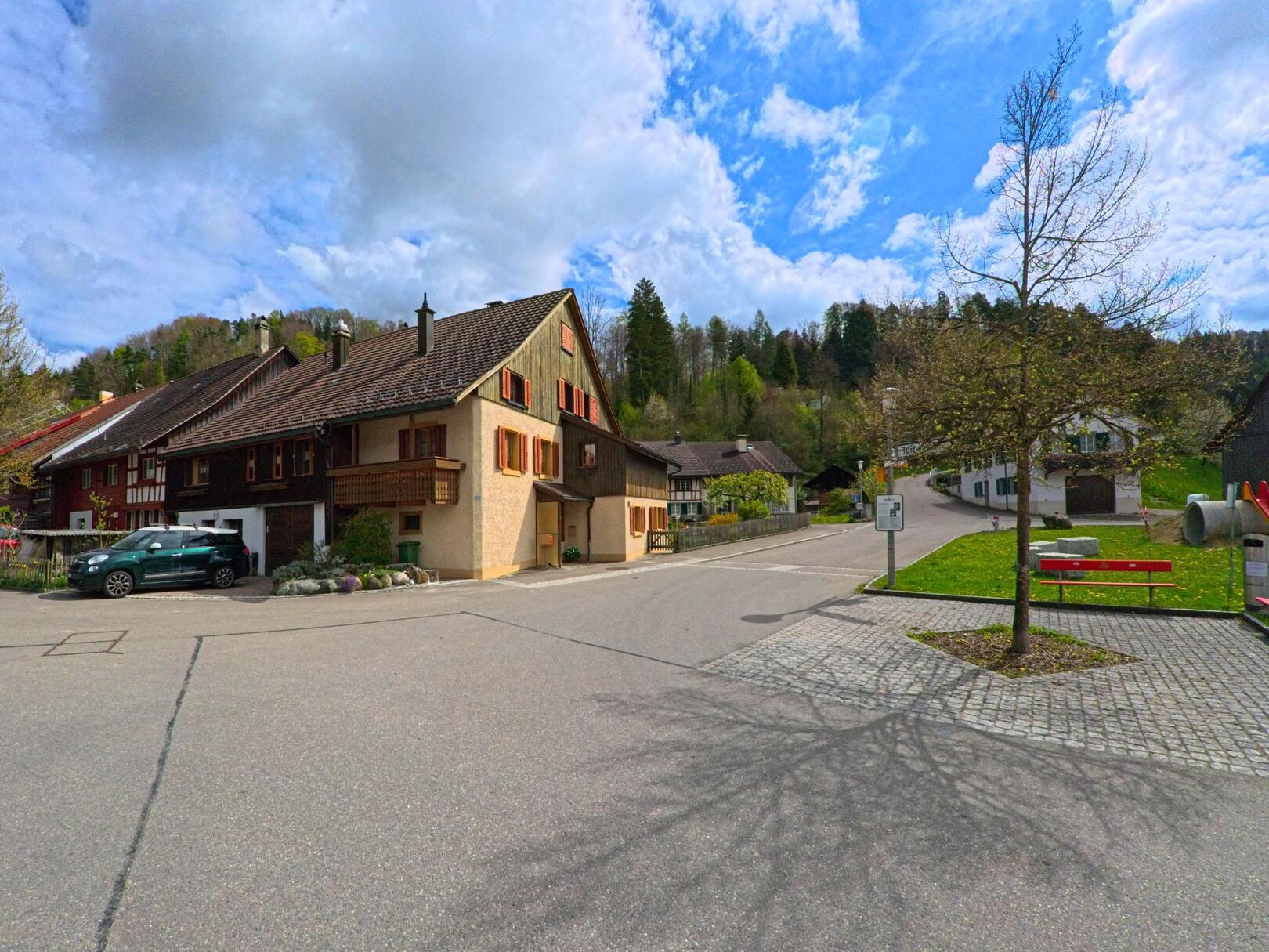 Im Ortszentrum von Zell (ZH, 8487, Kanton Zürich) stehen traditionelle Wohnhaeuser mit Holzfassaden an einer ruhigen Strassenkreuzung.