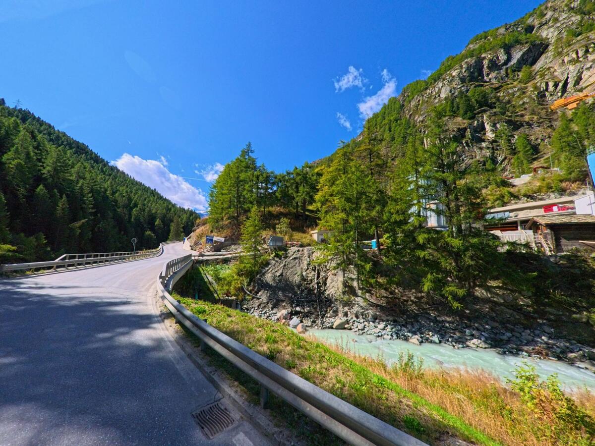 Eine Strasse fuehrt in Zermatt (3920, Kanton Wallis) ueber eine Bruecke, waehrend unten ein klarer Bergbach entlang der bewaldeten Haenge fliesst.