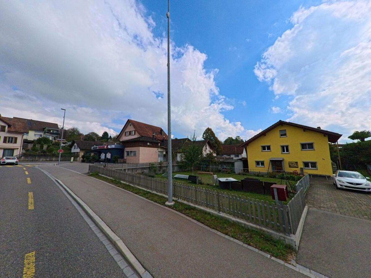 In Zetzwil (5732, Kanton Aargau) steht ein gelbes Wohnhaus mit umzäuntem Garten an einer leicht gebogenen Strasse neben weiteren Dorfhäusern.