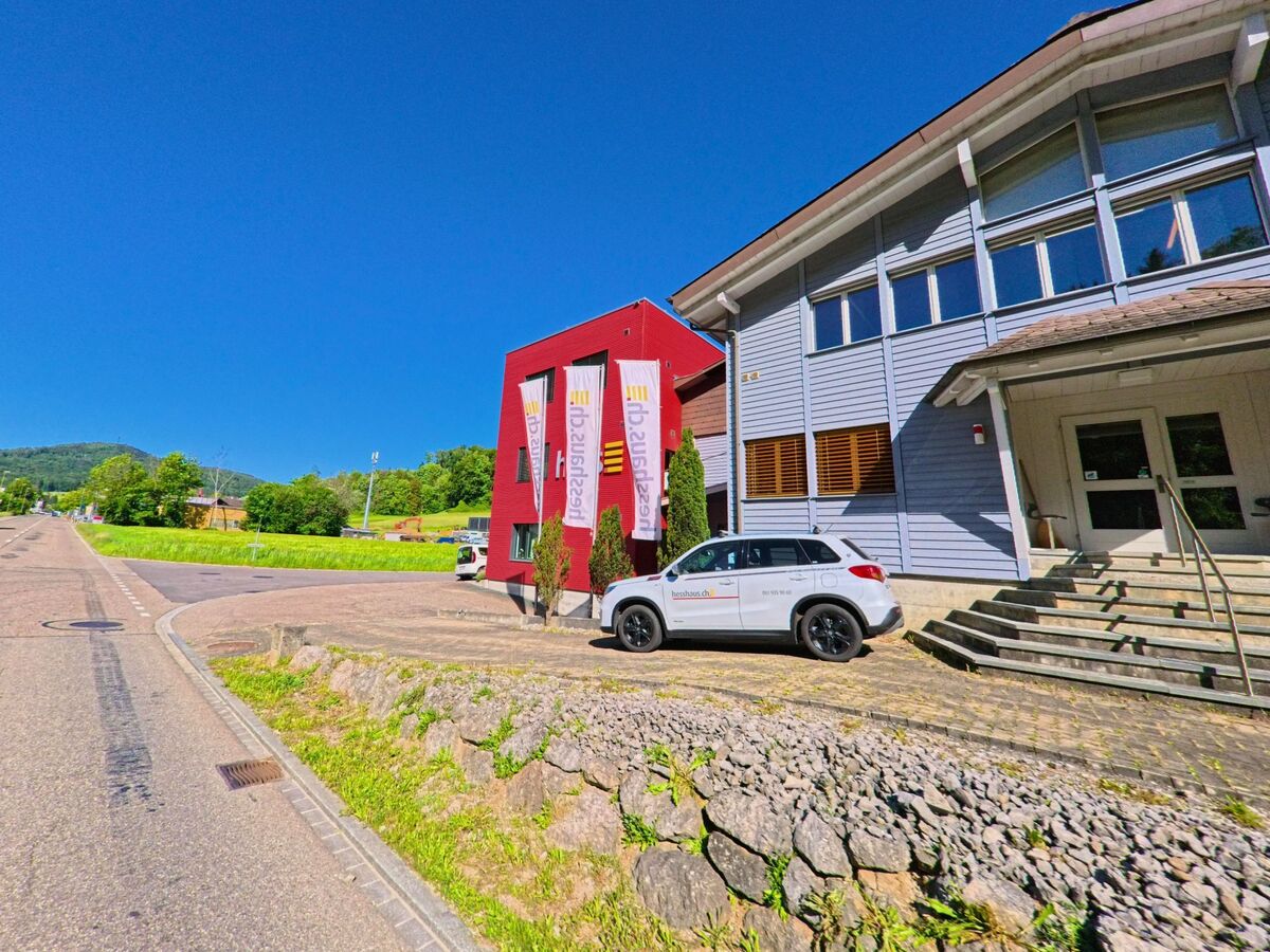 In Ziefen (4417, Kanton Basel-Landschaft) befindet sich ein modernes Gewerbegebäude mit Firmenbeschriftung und farbigen Fassaden direkt an der Hauptstrasse.