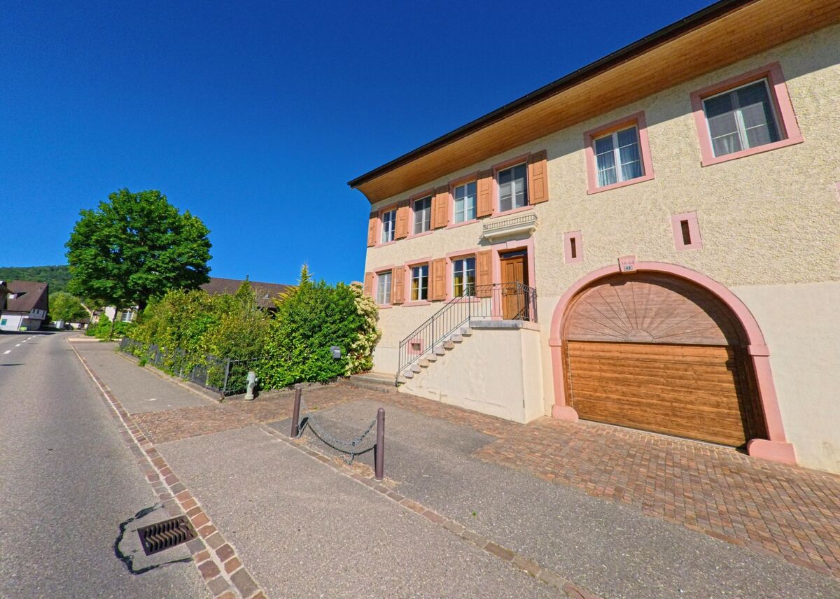 Ein gepflegtes Wohnhaus mit rosafarbenen Fensterrahmen und grosszügigem Tor prägt das Strassenbild in Ziefen (4417, Kanton Basel-Landschaft).