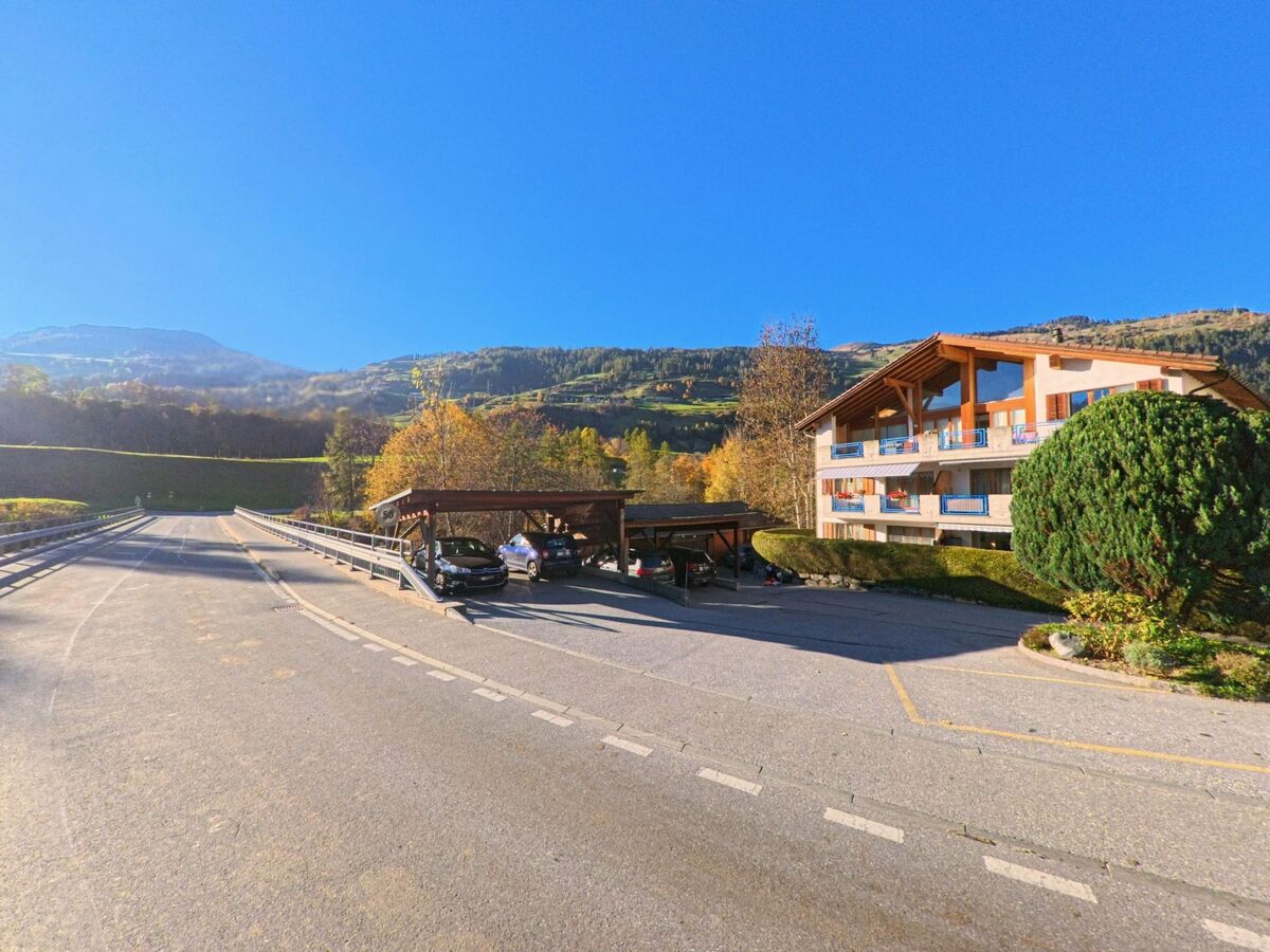 Entlang einer ruhigen Strasse mit Parkplätzen und Wohnbauten zeigt sich in Zillis-Reischen (7432, Kanton Graubünden) eine offene Siedlungslage vor herbstlich gefärbten Hängen.