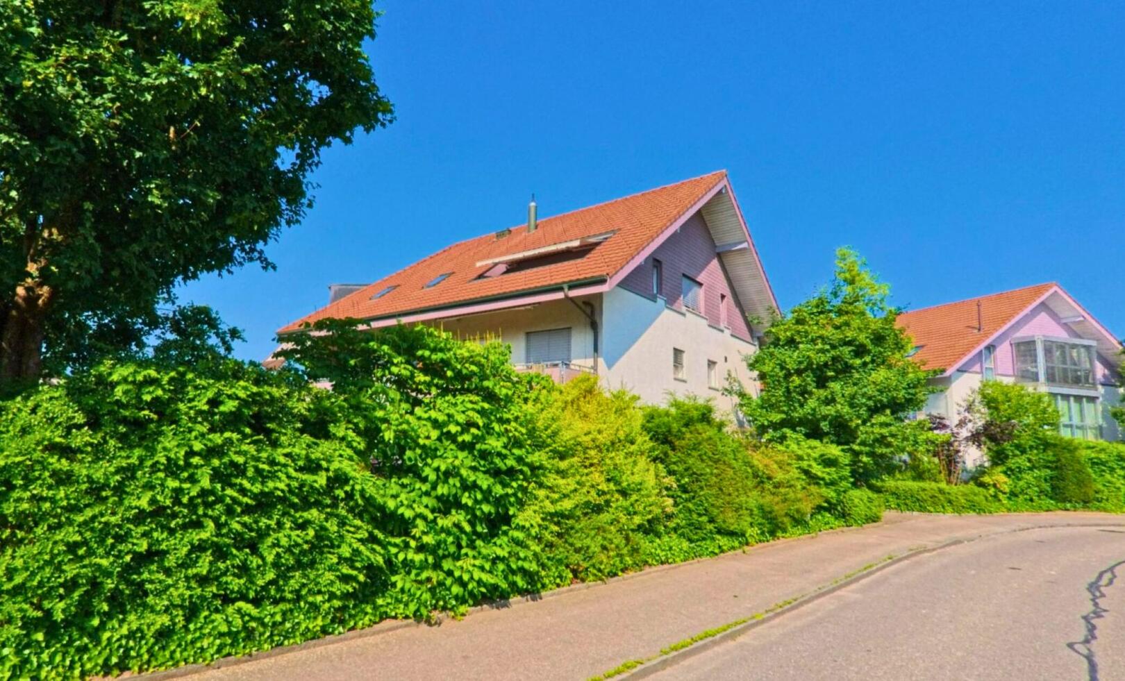 In der Gemeinde Zollikofen (3052, Kanton Bern) verläuft eine leicht ansteigende Wohnstrasse vorbei an gepflegten Einfamilienhäusern mit roten Ziegeldächern und üppiger Begrünung.