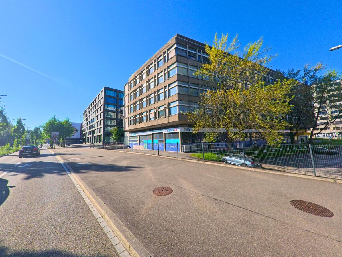 In Zürich, 8010 im Kanton Zürich reiht sich ein Spitex-Gebäude mit älterer Fassade an moderne Neubauten entlang einer ruhigen Quartierstrasse mit vereinzelten Autos.