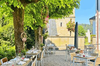 Unter grossen Baeumen ist in Schoeftland (5040, Kanton Aargau) ein Aussenbereich mit gedeckten Tischen und Blick auf eine historische Steinmauer eingerichtet.