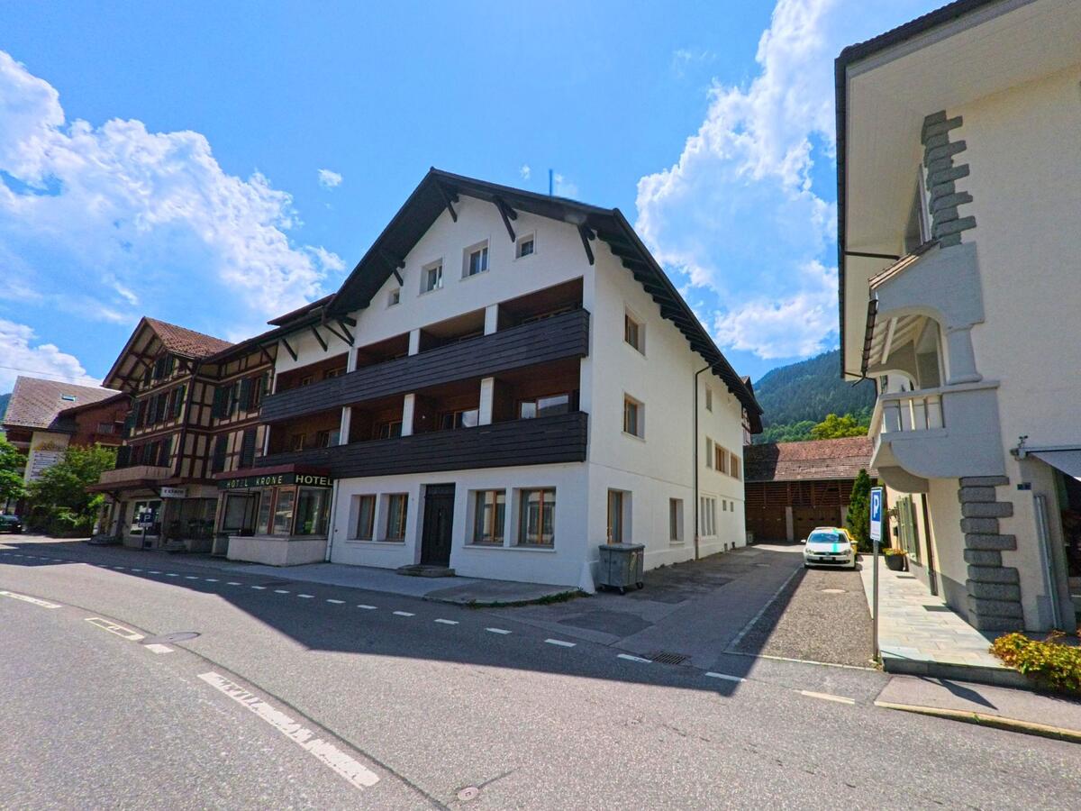 In der Ortsmitte von Zweisimmen (3770, Kanton Bern) liegt das Hotel Krone an einer gut ausgebauten Strasse, flankiert von traditionellen und modernen Gebaeuden vor bewaldeter Bergkulisse.