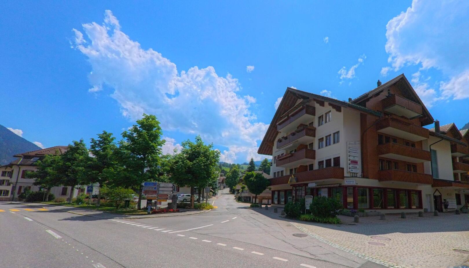 In Zweisimmen (3770, Kanton Bern) zweigt eine gepflasterte Strasse mit Wohn- und Geschaeftshaeusern an einer Kreuzung mit Wegweisern in ein ruhiges Wohnquartier ab.