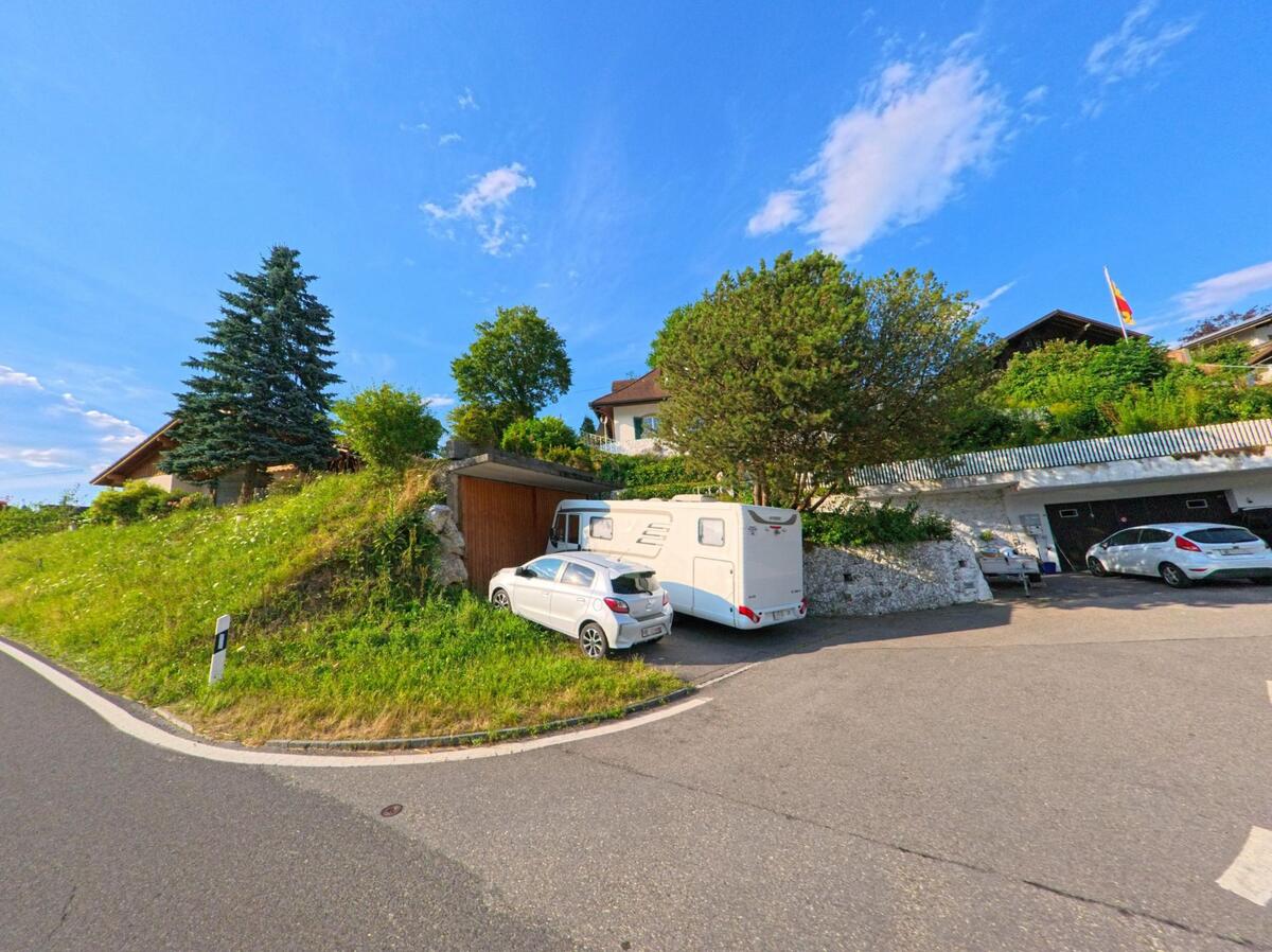 In Zwieselberg (PLZ 3645, Kanton Bern) stehen an einer Hangstrasse mehrere Fahrzeuge vor terrassierten Wohnhaeusern mit gepflegter Begruenung und einer wehenden Fahne.